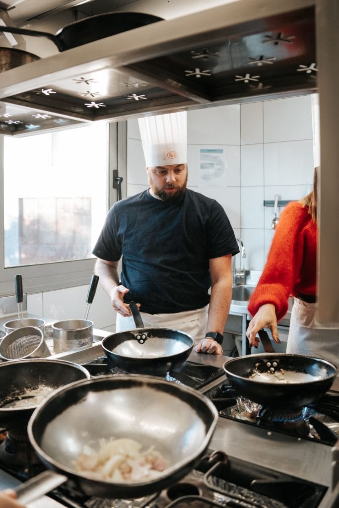 un monsieur avec une toque qui remue la poêle au cours de cuisine